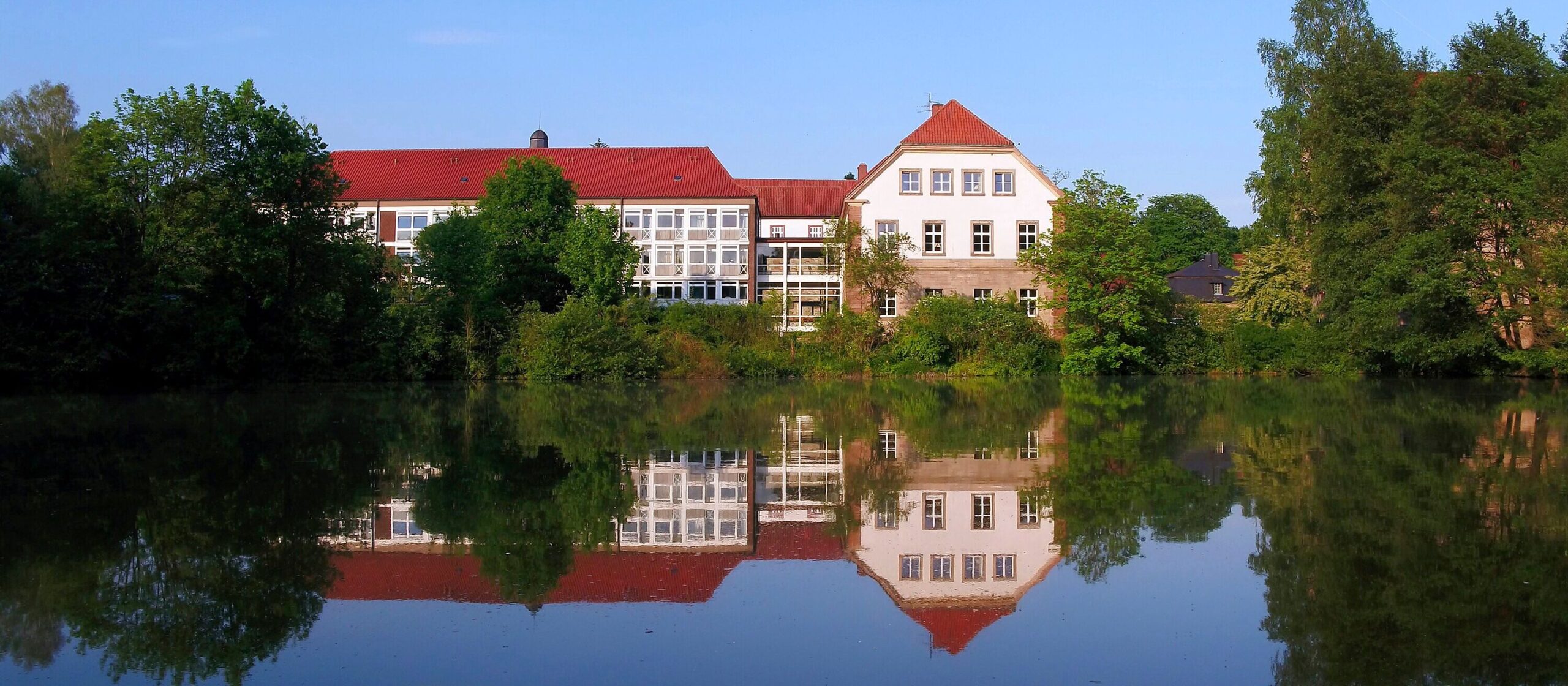 Gebäude der Landvolkshochschule Hardehausen, davor ein See, worin sich das Gebäude spiegelt