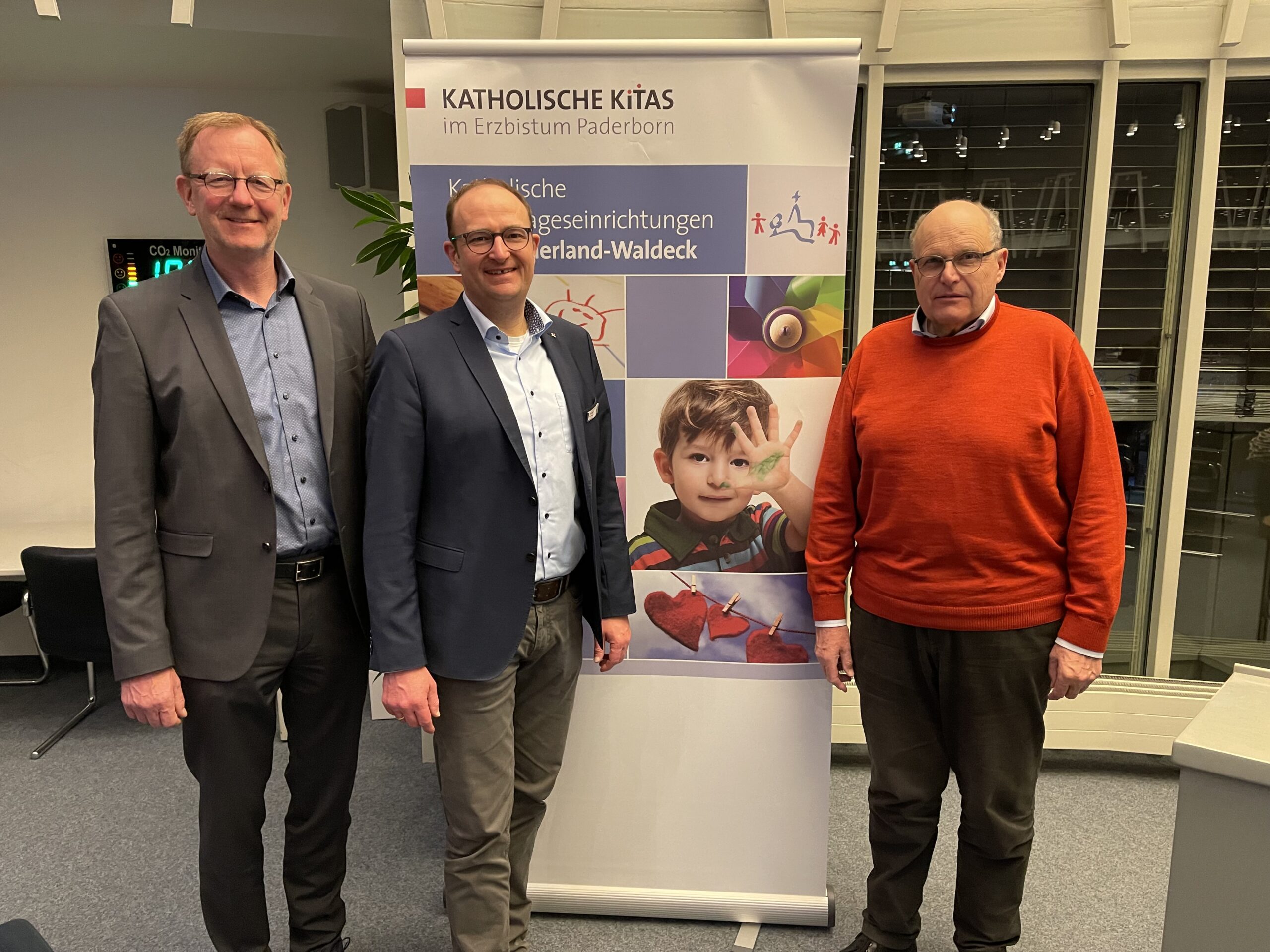 Drei Männer vor einem Banner mit der Aufschrift "Katholische Kitas"