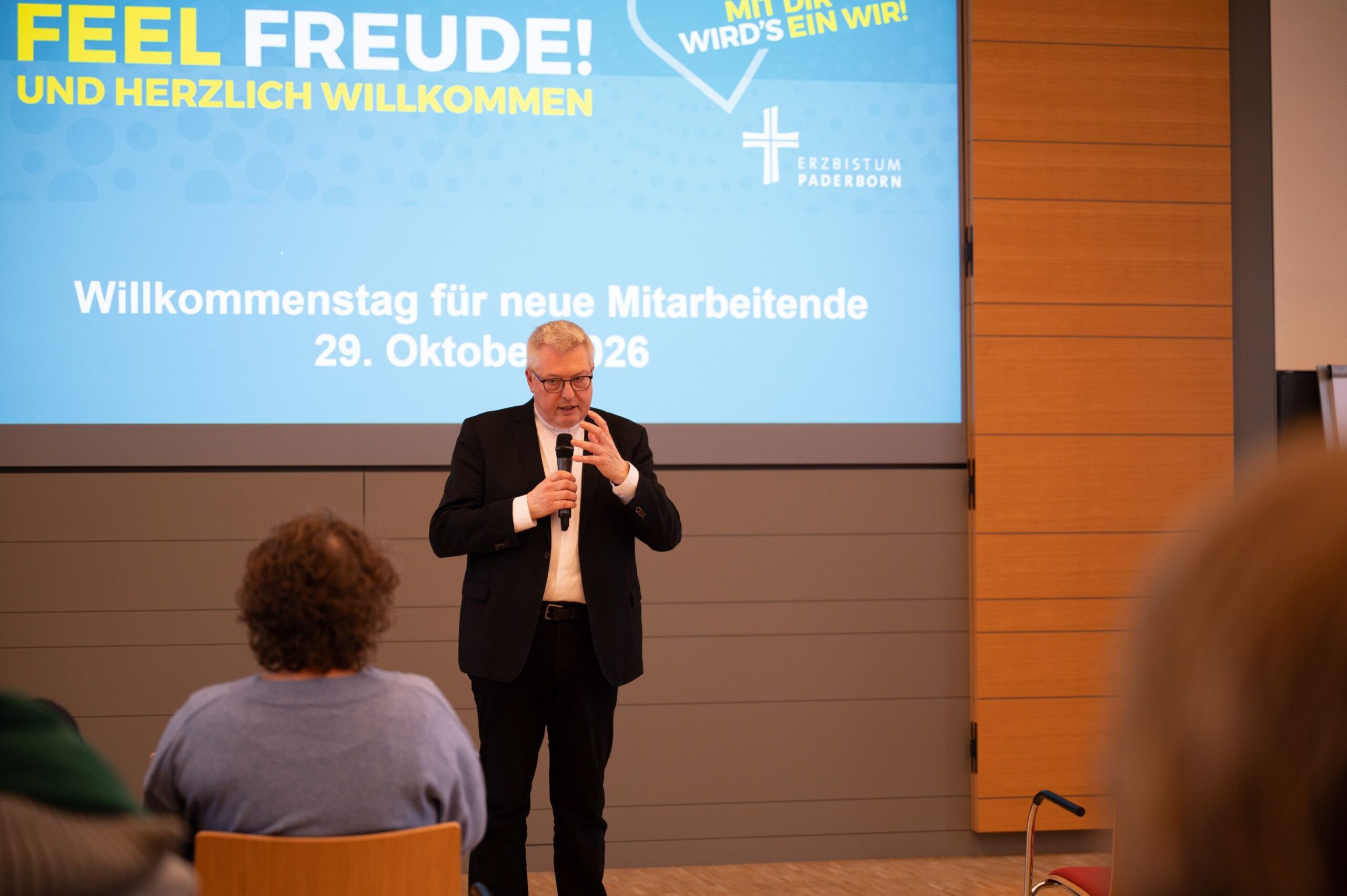 Ein Priester steht am Mikrofon vor einer Wand